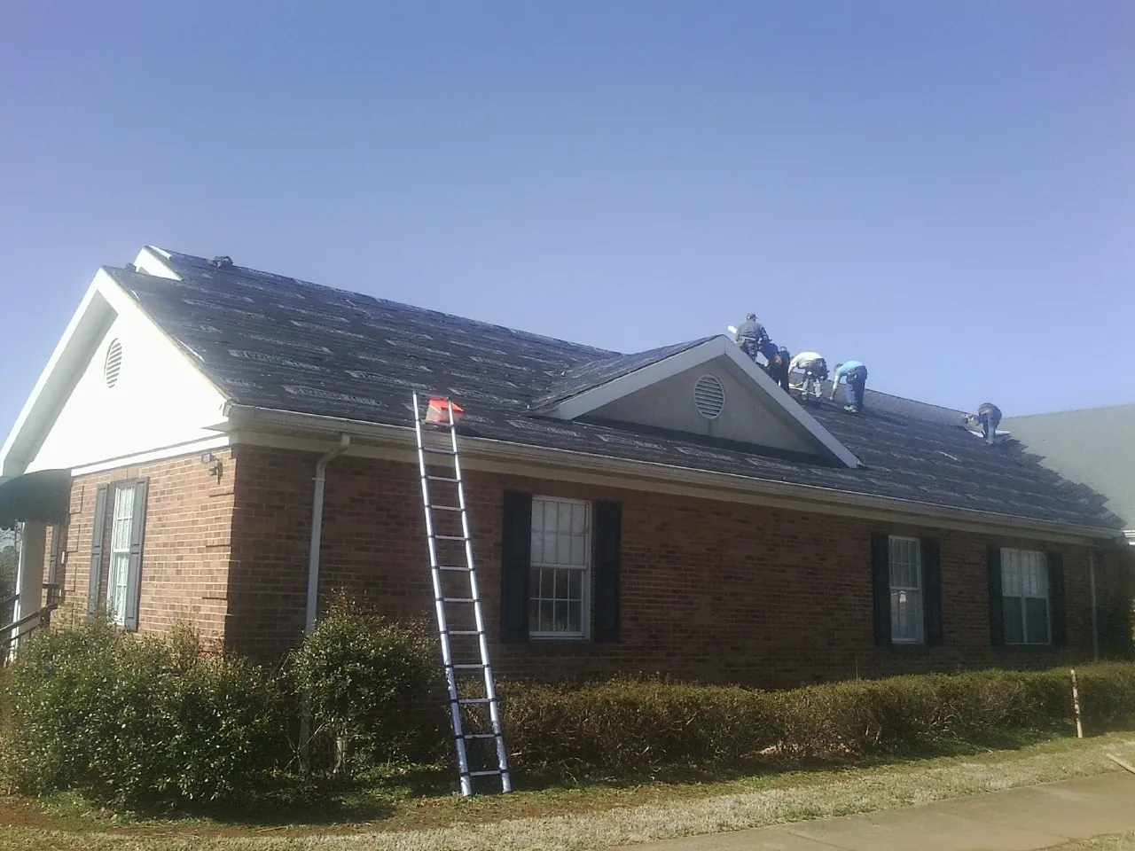 Crew tearing shingles off a brick ranch roof with a ladder set — Metal Roof Repair work by our crew in Phillipsport