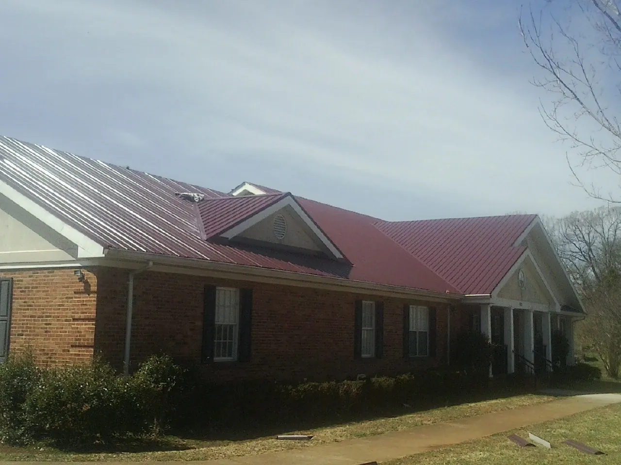 Red metal roof with gabled entries on a long brick building, from a Hail Damage Roof Repair job in Phillipsport