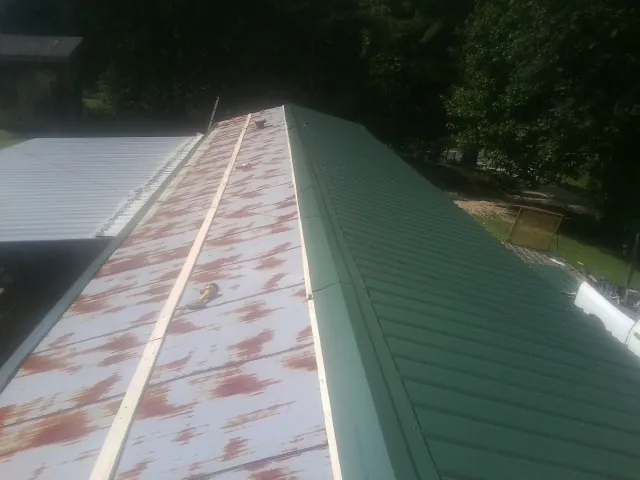Old rusted panels beside newly installed green metal roofing — Wind Damage Roof Repair by Roofing Brothers in Phillipsport