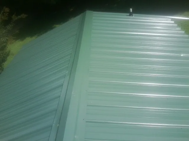 New green metal panels meeting at the ridge of a roof — Flat Roof Repair work by our crew in Phillipsport
