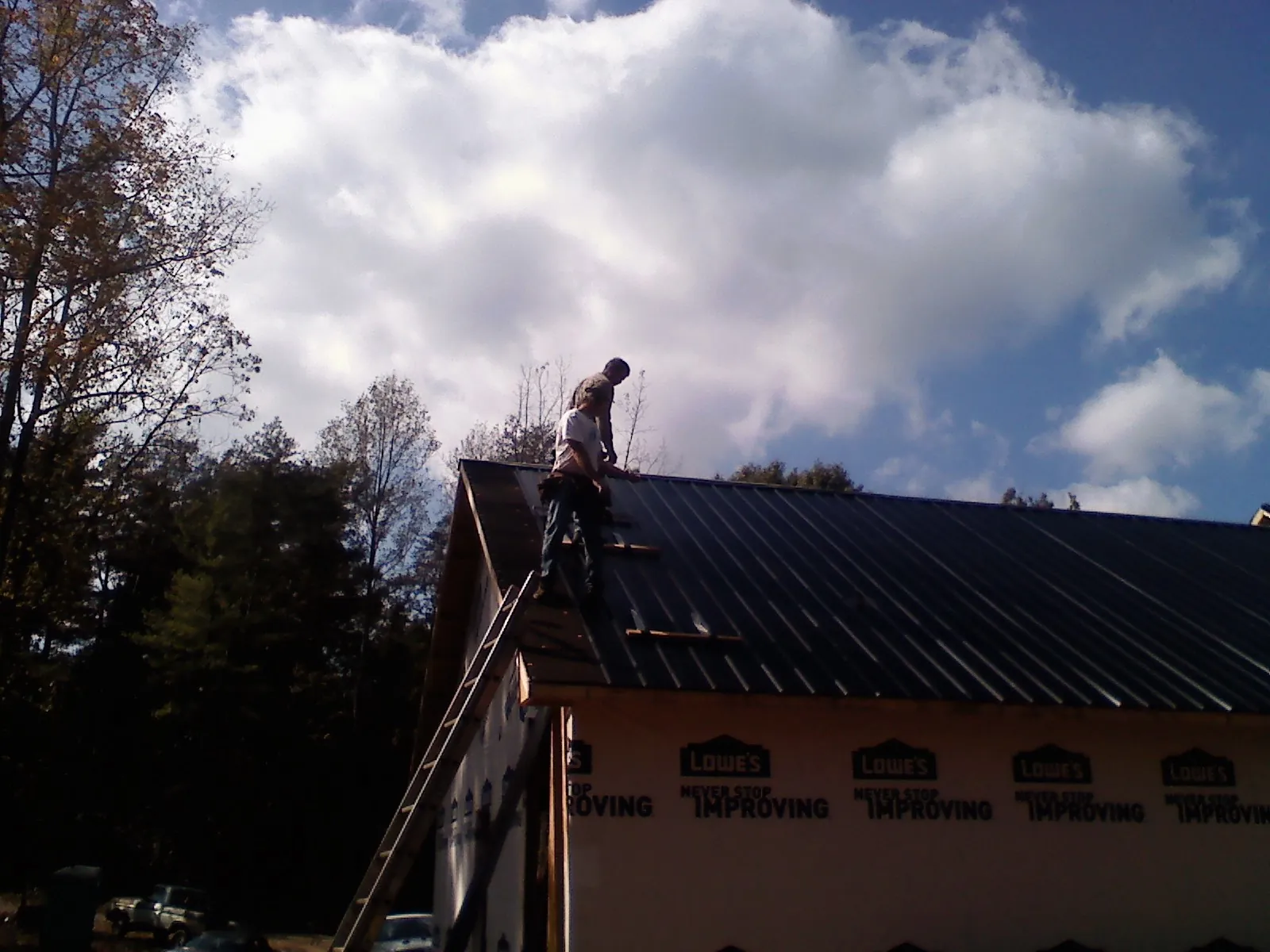 Roofer fastening dark metal panels high against a cloudy sky, from a Roof Inspection job in Phillipsport