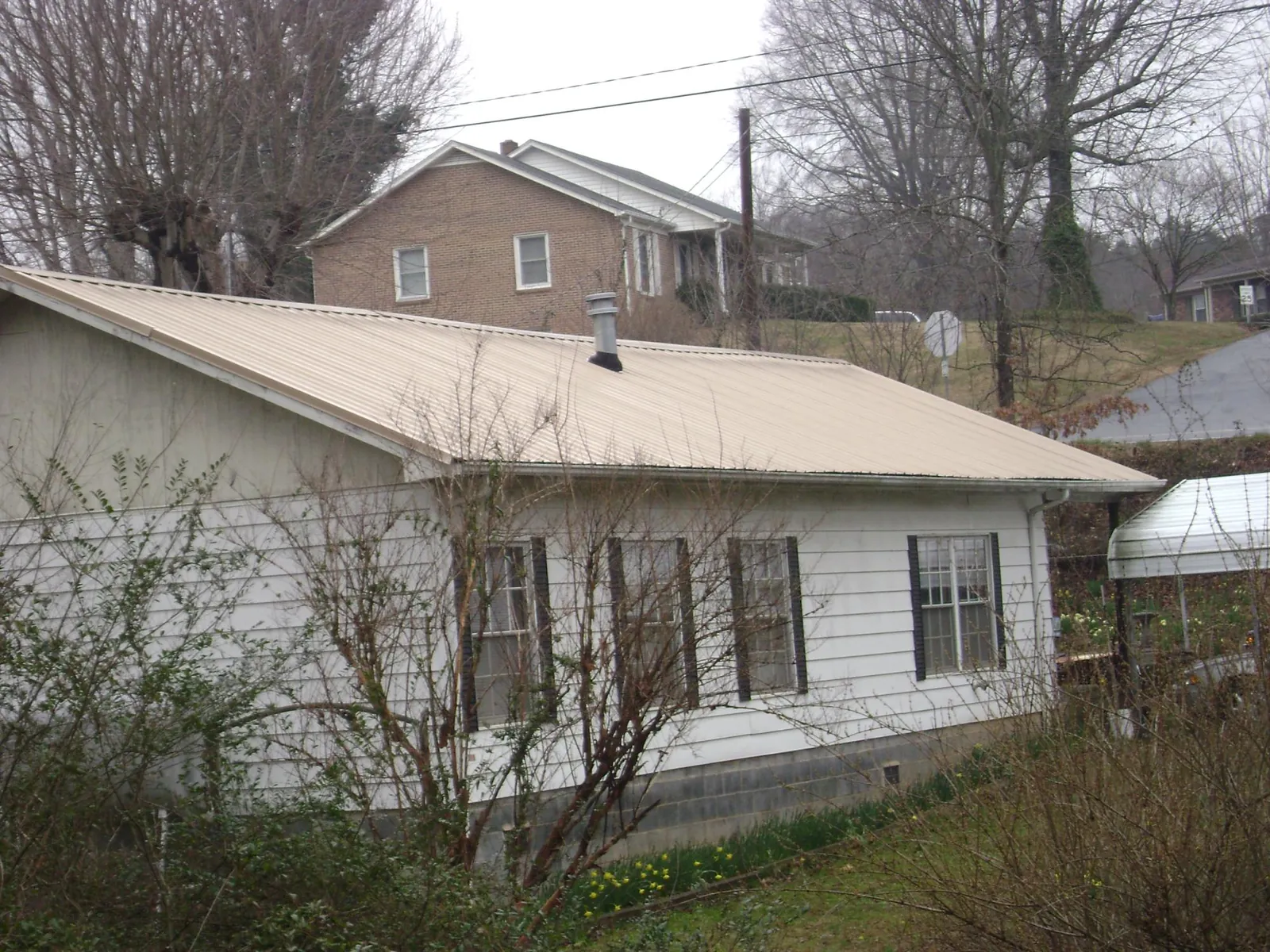 Tan metal roof on a white sided house set into a hillside — Commercial Roofing by Roofing Brothers in Phillipsport