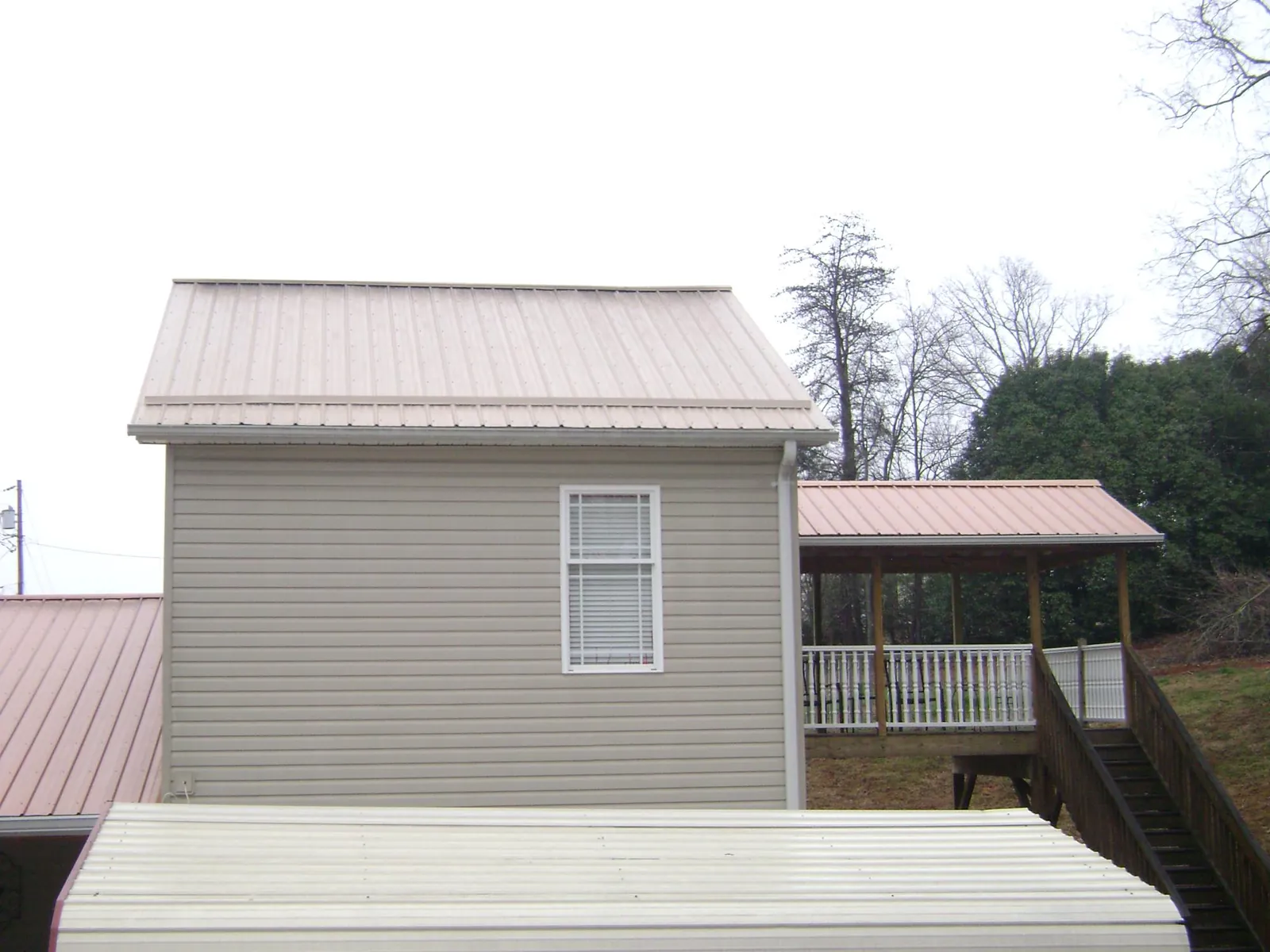Tan metal roofs on a two story addition and attached porch, from a Roof Replacement job in Phillipsport